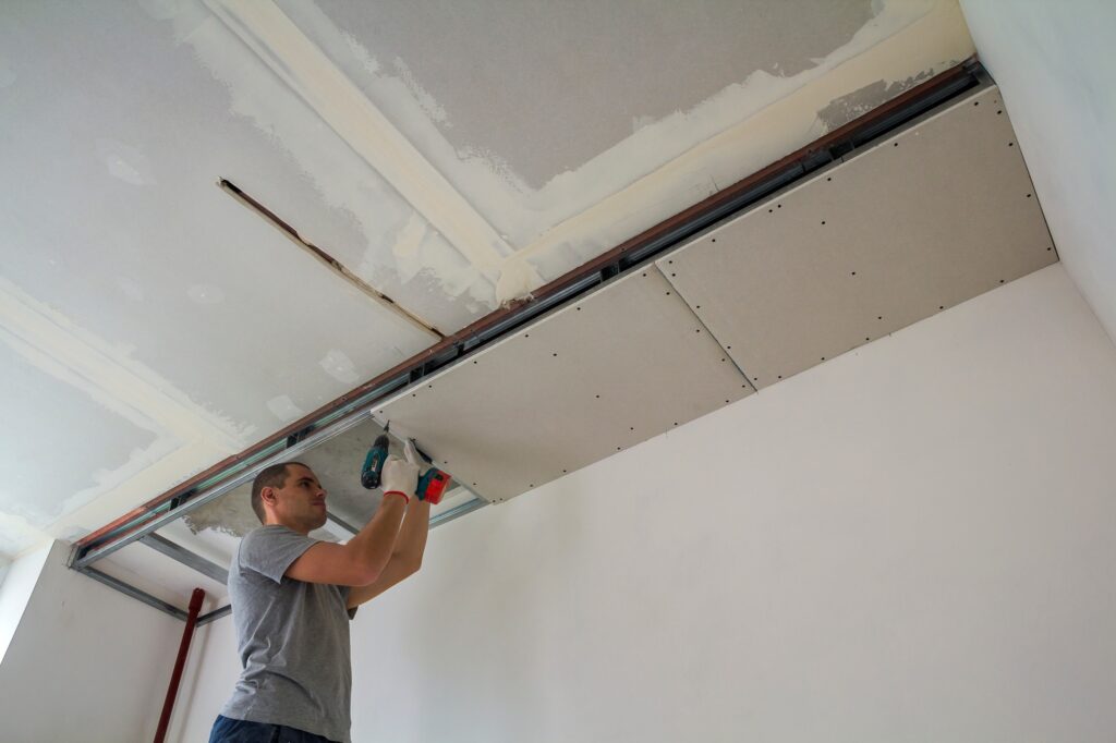 Construction worker assemble a suspended ceiling with drywall and fixing the drywall to the ceiling